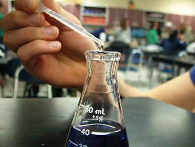 chemistry student adding chemical to beaker