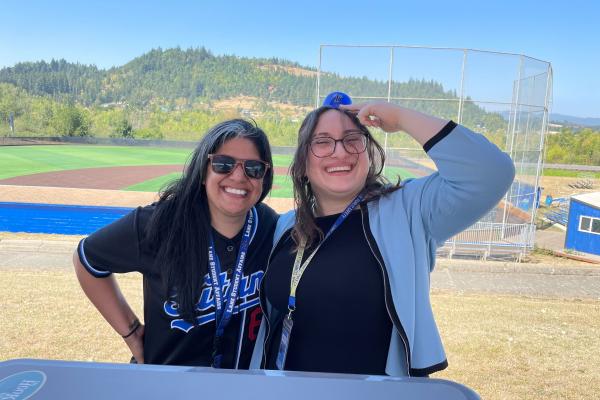 two admissions employees smile and pose together in front of the baseball diamond
