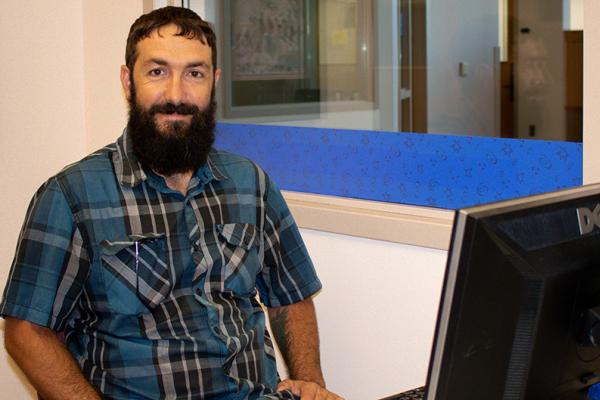 a student worker, a bearded young man, smiles as he submits his timesheet