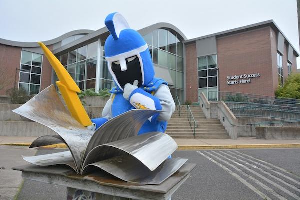 Ty the Titan mascot reads the book statue in front of building 1 and looks pensive