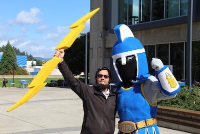 an employee poses with Ty the Titan Mascot, triumphantly holding his lightning bolt aloft