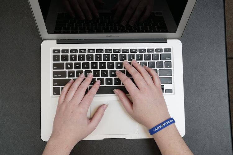 an employee wearing a Lane Titans bracelet using a MacBook Air computer