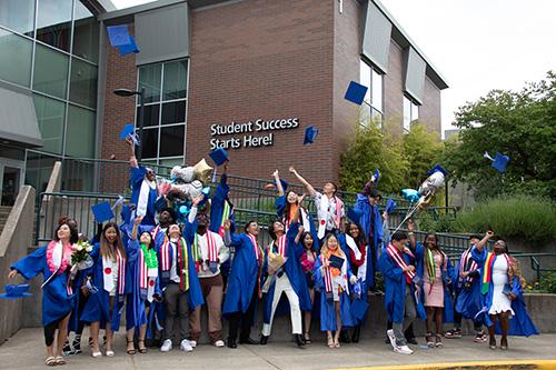 a group of about 30 international students from different countries wearing blue caps and gowns throwing their caps in the air happily