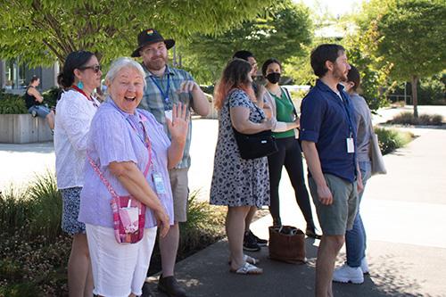 Staff members watching lawn games in summer at Classified Appreciation Day. An older woman smiles and waves at the camera.