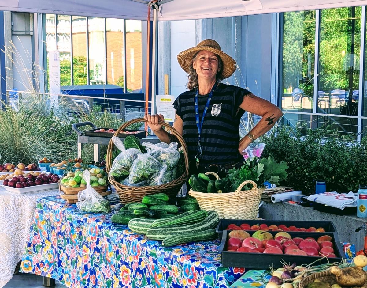 Learning Garden Coordinator Andrea Mull smiles as she poses next to summer produce like zucchini and tomatoes at a pop up market