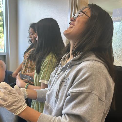 A Latina student throws her head back and laughs while making calveras with friends at the Multicultural Center