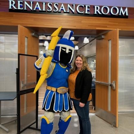 an LCC employee smiles and poses with Ty the Titan in front of the Renaissance Room